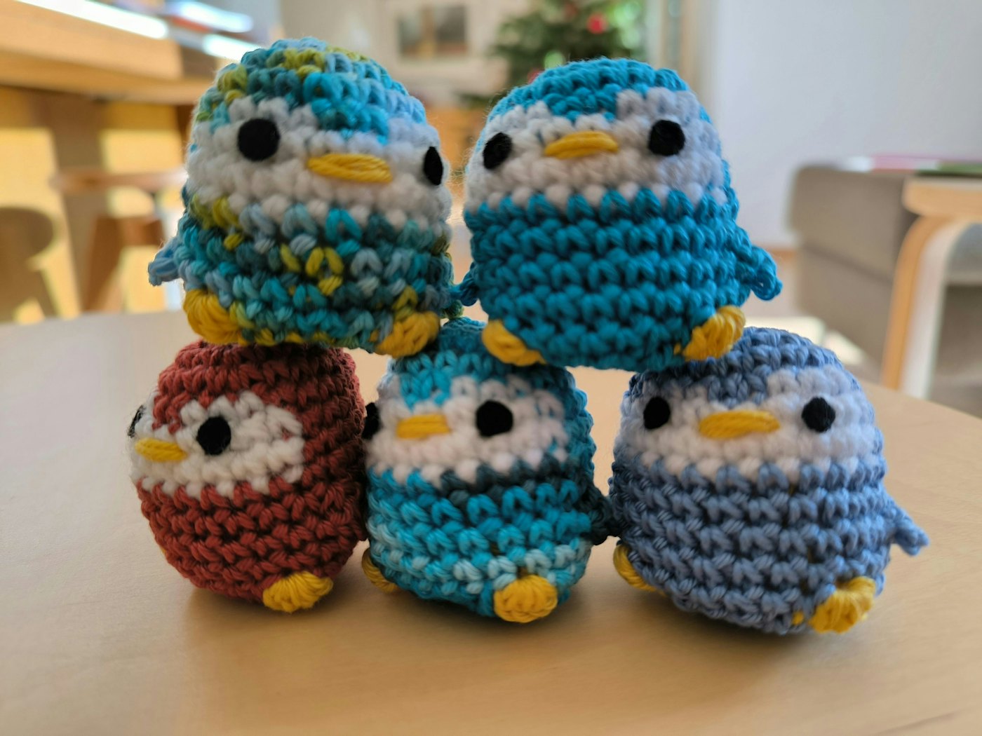 Five small crocheted amigurumi penguins stacked on a table