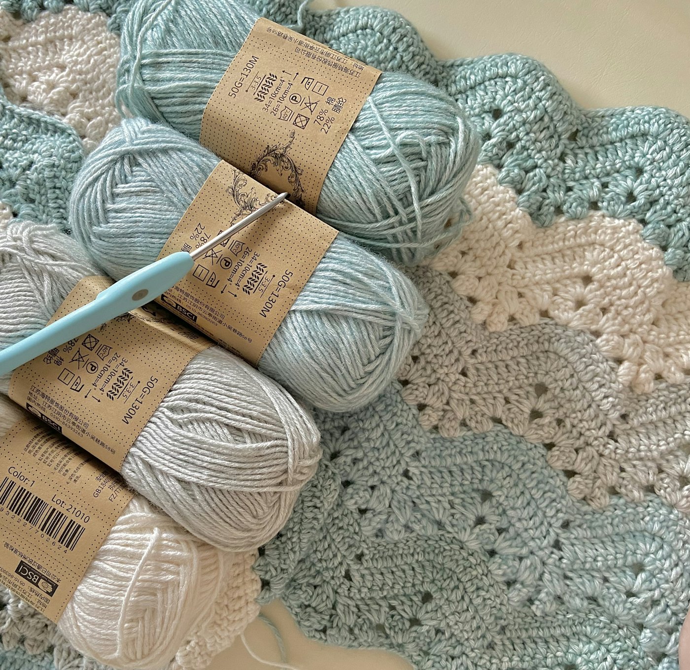 Skeins of mint and white yarn and a crochet hook on a chevron crochet blanket