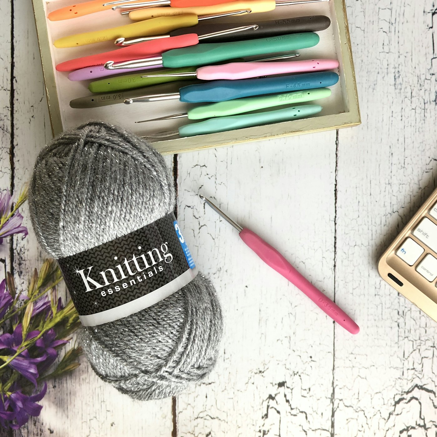 A set of colored crochet hooks beside a skein of grey yarn