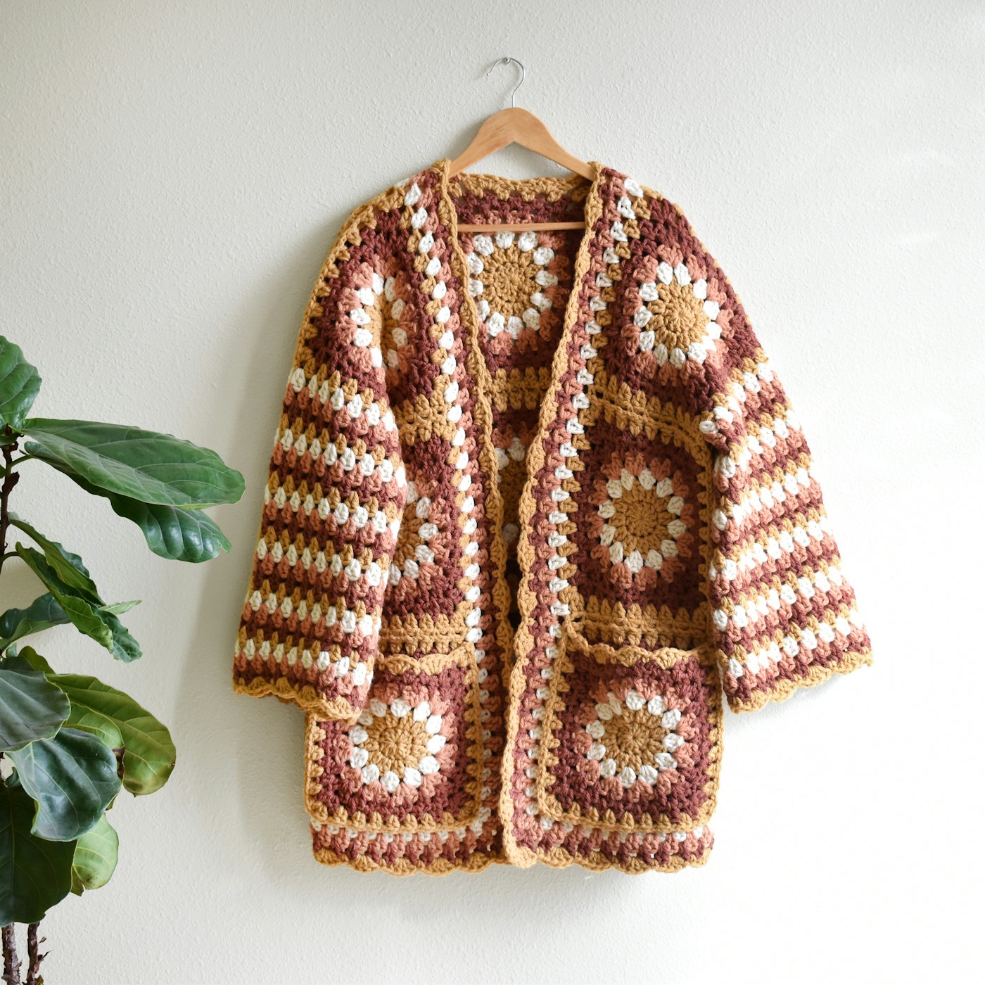 A handmade granny square crochet cardigan hanging on a wall
