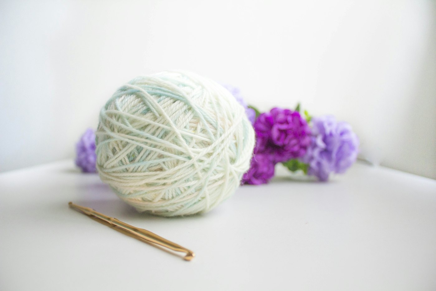 A ball of white yarn with lilac flowers and a crochet hook