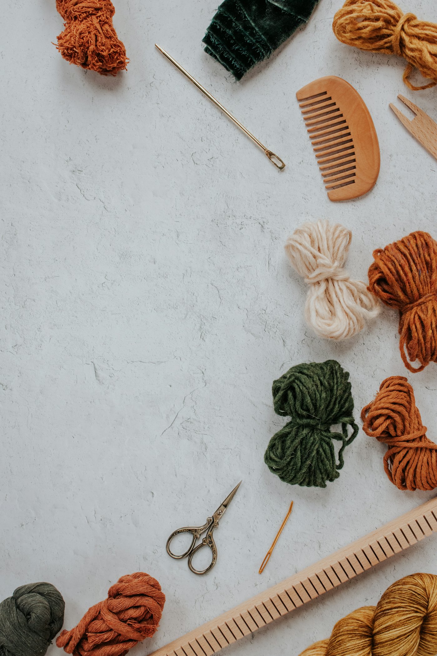 Bundles of rust, cream and green yarn on a grey surface