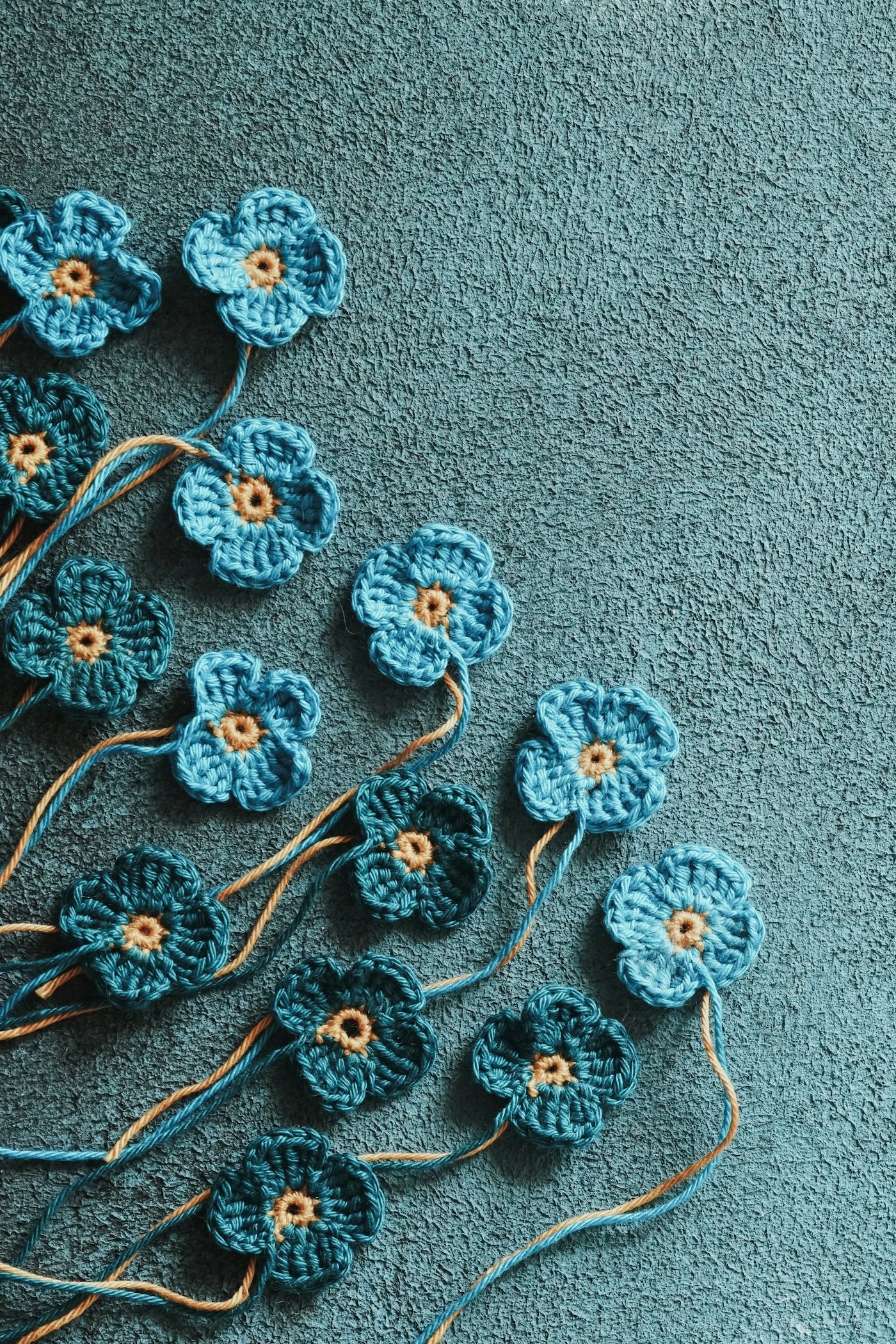 Small blue crocheted flowers on a teal surface