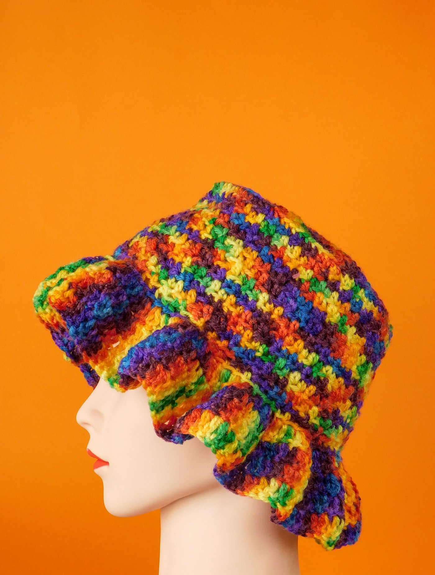 A crocheted bucket hat in rainbow stripes on an orange background